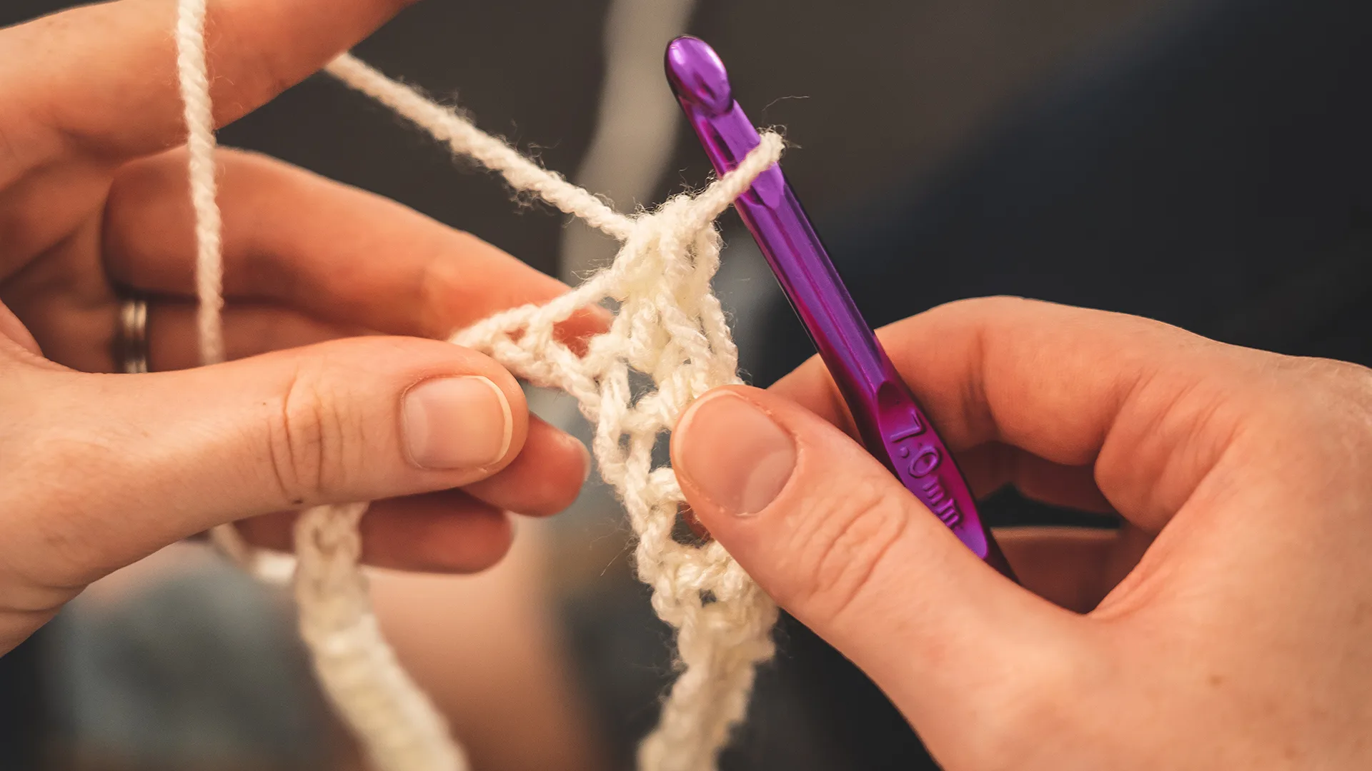 hands crocheting white yarn with purple hook