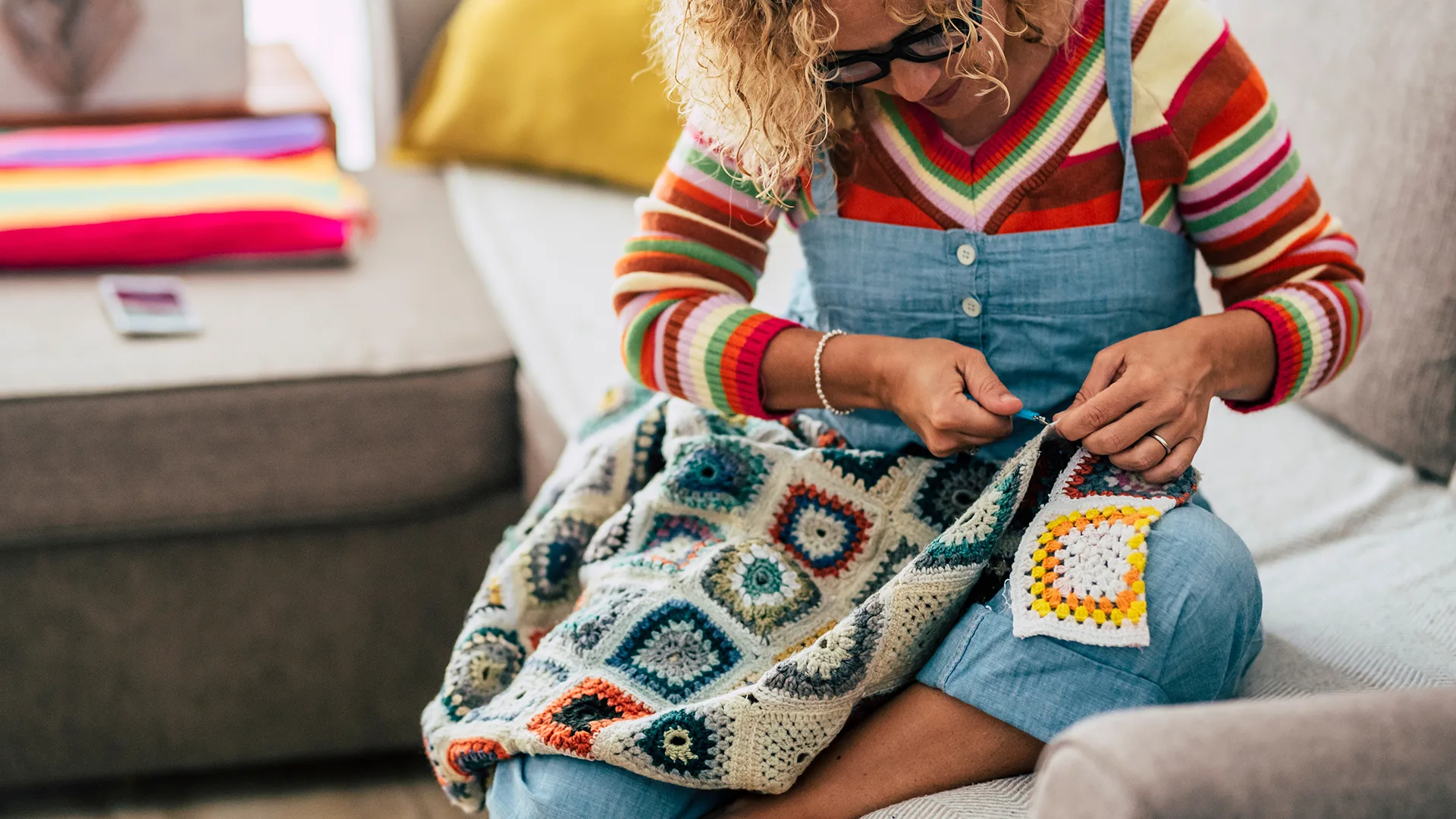 Woman-crocheting-blanket-living-room.webp